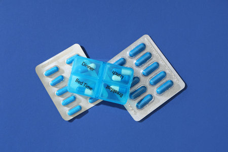 Pill organizer and capsules on blue background. Top view