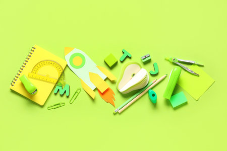 Different school stationery and paper rocket on green background
