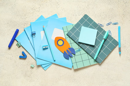 Paper rocket with copybooks and different stationery on white grunge background. Top view