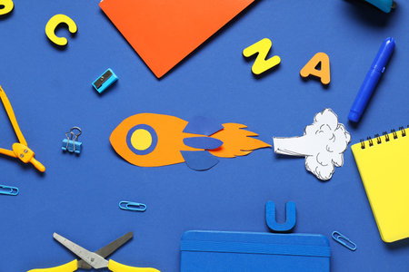 Paper rocket with smoke and different school stationery on blue background