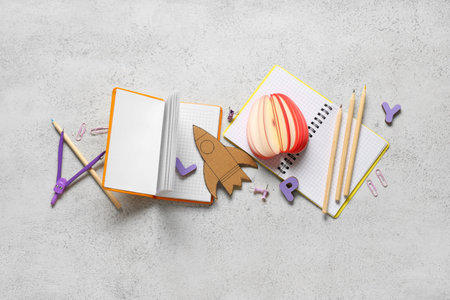 Paper rocket with notebooks and different stationery on white grunge background. Top view