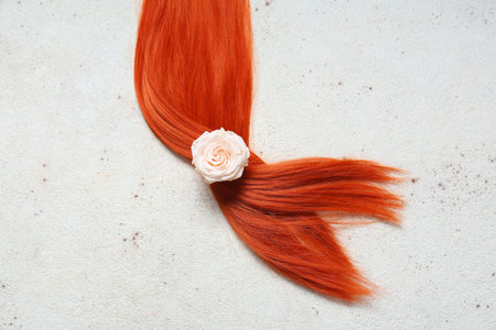 Red hair strand with rose flower on light backgroundの写真素材