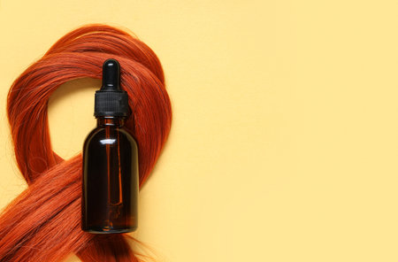 Red hair strand and bottle of cosmetic product on pale yellow backgroundの写真素材