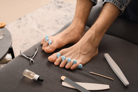 Feet of young man with tools, toe separator and fresh pedicure at home, closeupの写真素材
