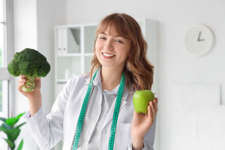 Female nutritionist with broccoli and apple in officeの写真素材