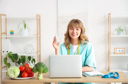 Female nutritionist with glass of water at table in kitchenの写真素材