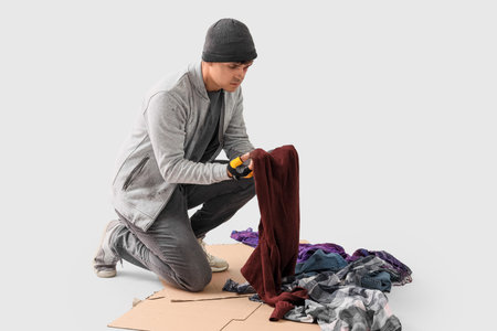 Young homeless man with clothes on light backgroundの写真素材