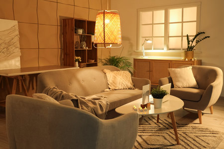 Interior of living room with cozy sofa, armchairs and glowing lampsの写真素材