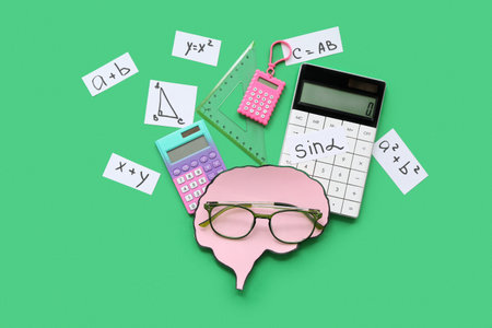 Paper brains with eyeglasses, math formulas and equations, calculators and triangle ruler on green backgroundの写真素材