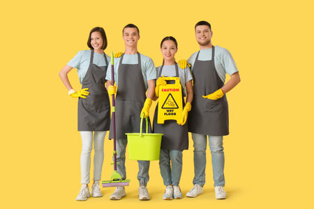 Group of young janitors with cleaning supplies on yellow backgroundの写真素材