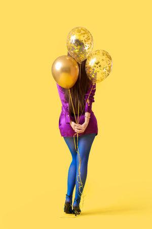 Young woman with air balloons on yellow background, back viewの写真素材