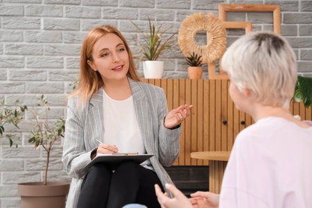 Female psychologist with clipboard talking to teenage girl in officeの写真素材