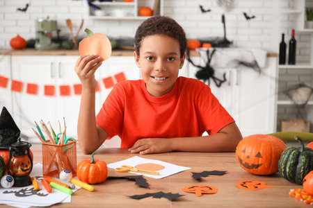 Teenage African-American boy with paper pumpkin making Halloween decorations at homeの写真素材