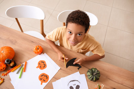 Teenage African-American boy cutting paper witch hat for Halloween decorations at home, top viewの写真素材