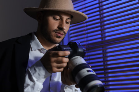 Male detective with photo camera near window in room at night, closeupの写真素材