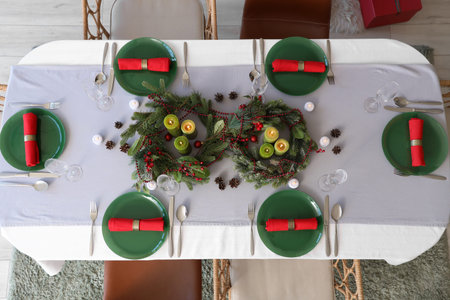 Christmas table setting with burning candles and wreaths in room, top view