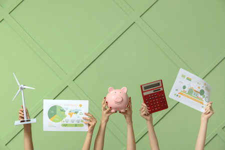 Many hands with wind turbine model, piggy bank and diagrams on color background. Green energy...