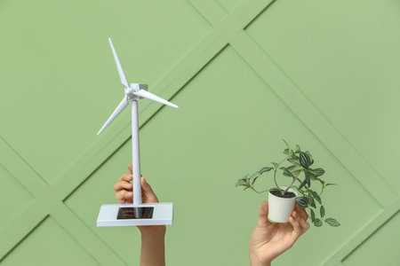 Female hands with wind turbine model and plant on color background. Green energy conceptの写真素材