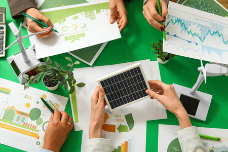 Business team with wind turbine models and solar panel working on green energy strategies during...
