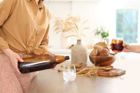 Young women with bread slices and spikelets pouring tasty kvass into glasses in kitchen, closeupの写真素材