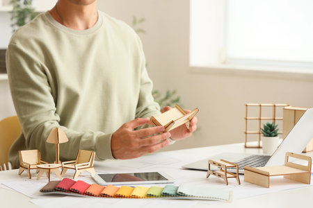 Male furniture designer with miniature model working at table in office, closeup
