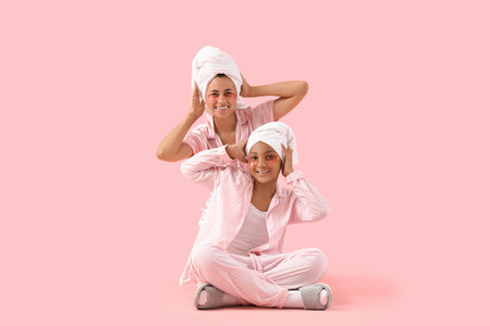 Happy young African-American mother and her daughter in pajamas after shower with under-eye patches on pink backgroundの写真素材