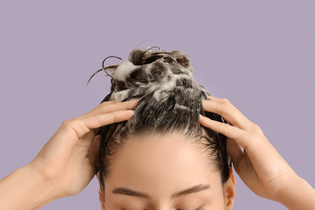 Beautiful young woman washing her hair with shampoo on purple background, closeupの写真素材