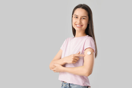 Diabetic young woman pointing at glucose sensor on light background