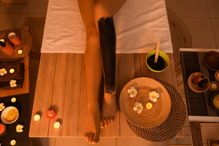 Young woman with mud on her leg in dark spa salon, top viewの写真素材