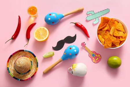 Composition with Mexican maracas, tasty nachos, chili peppers and decor on pink background. El Dia...