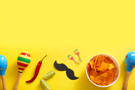 Composition with Mexican maracas, tasty nachos and decor on yellow background. El Dia de Muertos