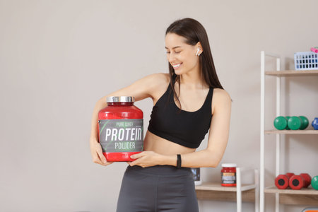 Sporty young happy woman with jar of protein powder in gym