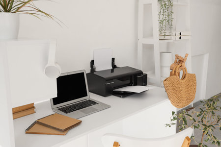 Modern printer with laptop on desk in light office