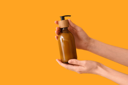 Female hands with bottle of cosmetic product on orange backgroundの写真素材
