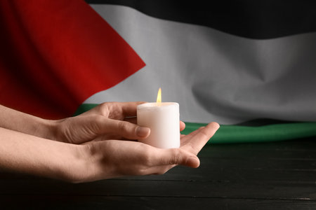 Hands holding burning candle and flag of Palestineの写真素材
