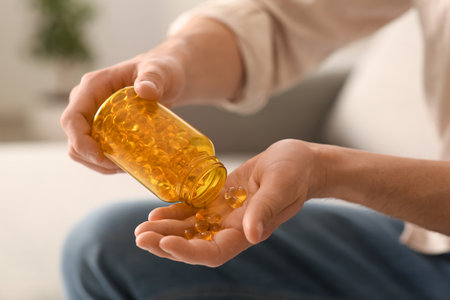 Handsome young man with jar of fish oil capsules at home, closeupの写真素材