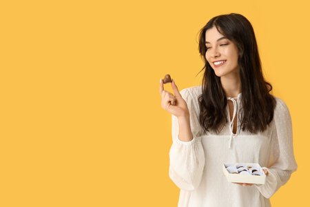 Young woman with box of delicious chocolate candies on yellow backgroundの写真素材
