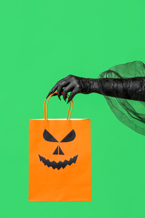 Black hand of witch with shopping bag on green background. Halloween celebrationの写真素材