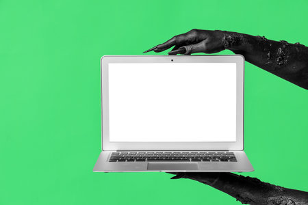 Black hands of witch with modern laptop on green background. Halloween celebrationの写真素材