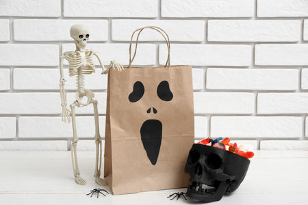 Paper shopping bag, decor and candies for Halloween on table against light brick wallの写真素材