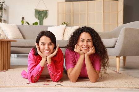 Young lesbian couple lying on carpet at homeの写真素材