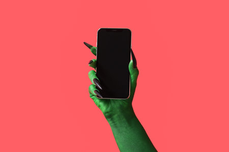 Green hand of witch with mobile phone on red background. Halloween celebration