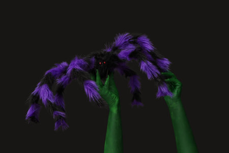 Green hands of witch with spider on black background. Halloween celebration