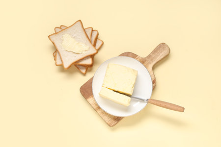 Wooden board with fresh butter and bread on color backgroundの写真素材