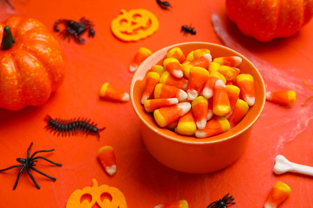 Composition with bowl of sweet candy corns and Halloween decorations on orange backgroundの写真素材