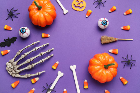 Frame made of Halloween decorations and sweet candy corns on purple background