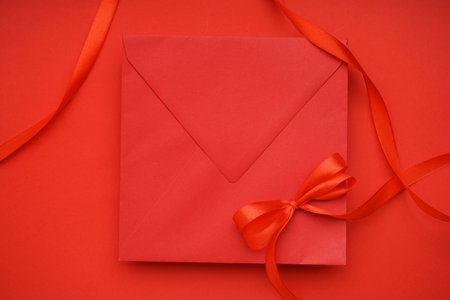 Envelope and bow made of satin ribbon on red backgroundの写真素材