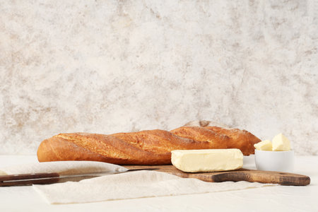 Wooden board with fresh butter, bread and knife on light tableの写真素材