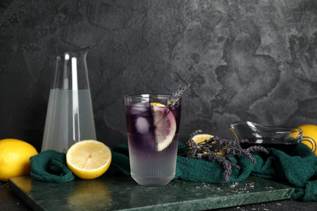 Composition with glass of cold lavender lemonade, flowers, lemons and syrup on dark background