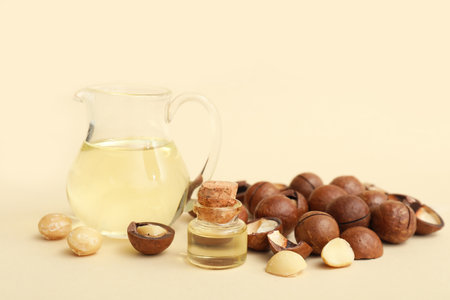 Bottle and jug with macadamia oil and nuts on beige background, closeupの写真素材
